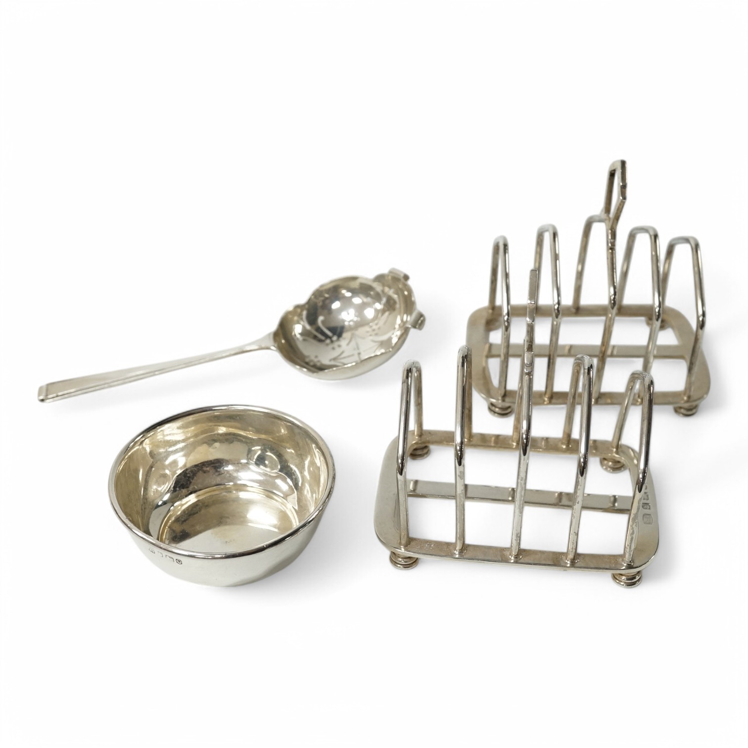 A pair of George V/VI silver five bar toast racks by Hukin & Heath, Birmingham, 1935/39, length 89mm, together with a silver tea strainer and stand, Sheffield, 1958, 9.1oz. Condition - fair to good